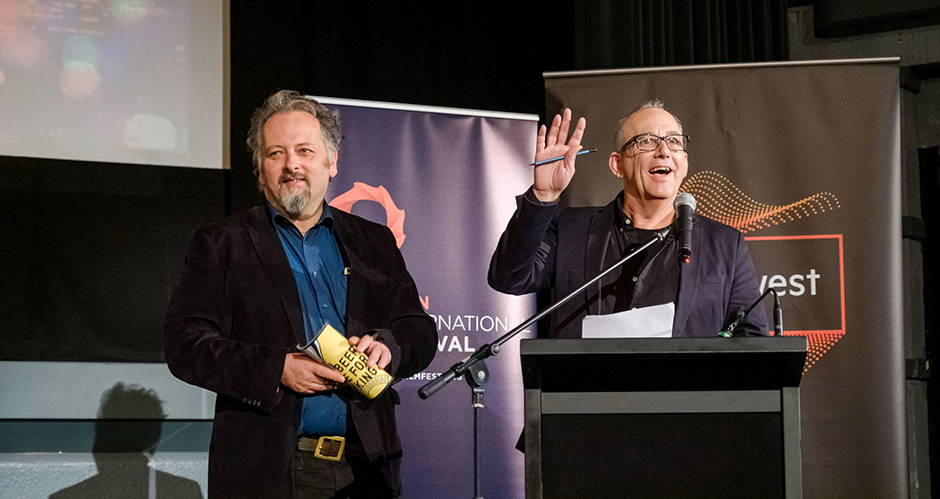 Program Director Jack Sargeant and Director and Found Richard Sowada in a cinema behind a lectern in a cinema, excitedly announcing the 2019 Revelation Film Festival Program.