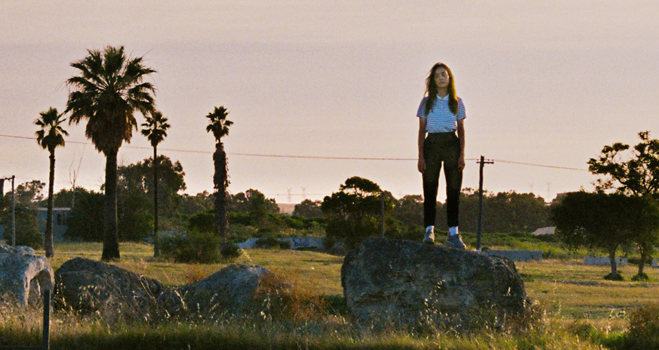 A girl girl standing on a rock looking forlorn at sunset.