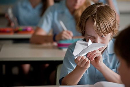 Ed Oxenbould as Dylan holding a paper plane in a classroom