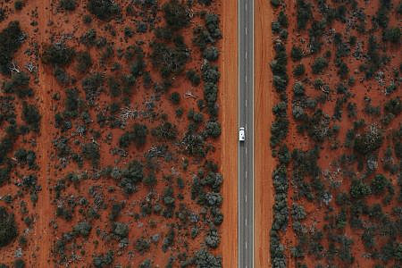 Aerial photos of white vehicle driving down a road surrounded by red earth and scrubland.
