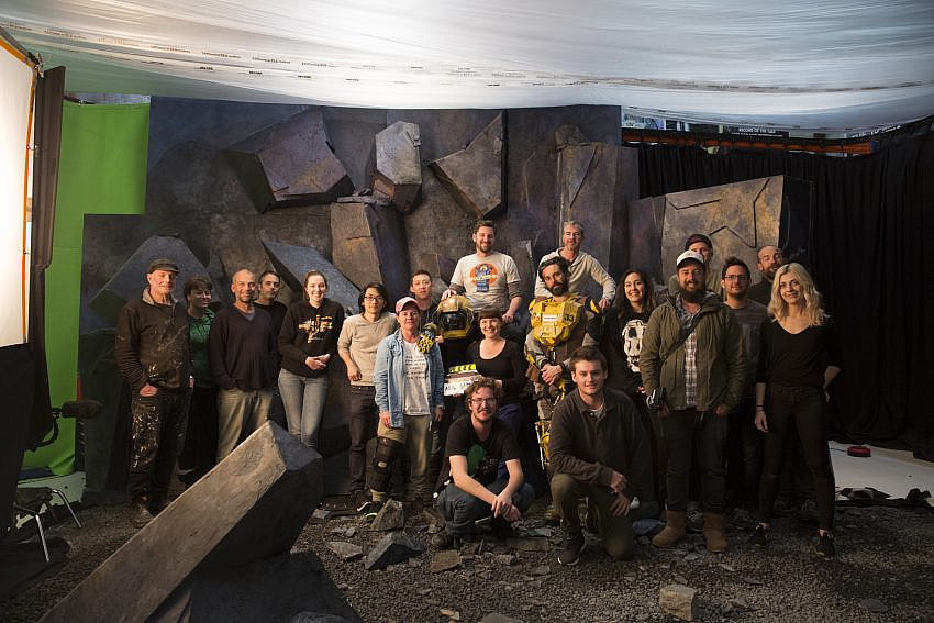 Cast and crew of Carmentis standing on the set of a rocky planet with a green screen in the background