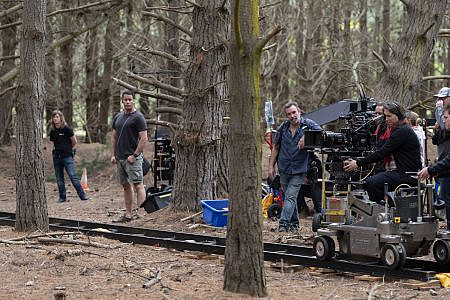 Camera operator on a tracking dolly surrounded by crew in a forest